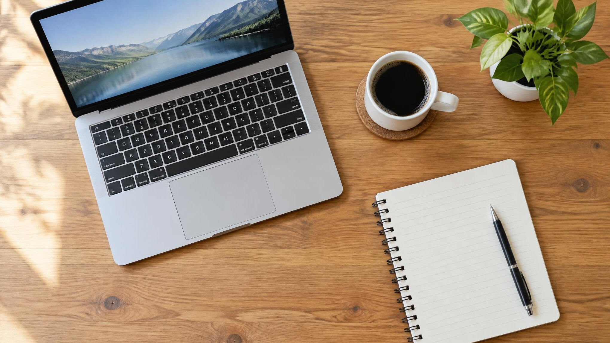 Desk with laptop, notebook, coffee cup and a small plant